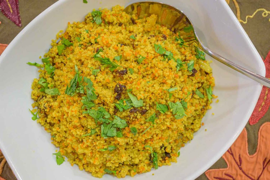 White bowl with savory turmeric couscous, almonds, raisins and chopped cilantro